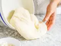 Frischer Teig, der aus einer Schüssel auf eine bemehlte Arbeitsfläche gleitet. Ähnlich wie Mehl Typ 0, ideal zum Backen.