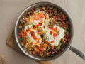Huevos al plato con verduras salteadas, pimientos, calabacín y berenjena, todo en una sartén.
