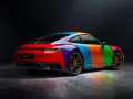 Porsche 911 Carrera GTS w tęczowym malowaniu, z pomarańczowymi felgami i odbiciami światła na podłożu.