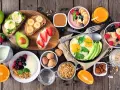 Mnóstwo pyszności na śniadanie: tosty z awokado i jajkiem, z masłem orzechowym i bananem, z serkiem i truskawkami, owsianka, jogurt z owocami, jajecznica, pomarańcza i sok.