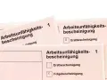Arbeitsunfall krankschreibung unterbrochen: Mehrere Arbeitsunfähigkeitsbescheinigungen liegen übereinander. Eine Folgebescheinigung ist angekreuzt.