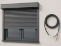 Szary, elektryczny system rolet zewnętrznych zamontowany na ścianie, obok zwinięty kabel z kolorowymi przewodami.