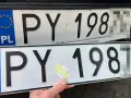 Dwie polskie tablice rejestracyjne PY 198. Jedna jest zamontowana na samochodzie, druga trzymana w ręku.