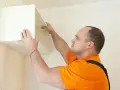 Un homme installe une étagère murale, une étape cruciale pour fixer meuble lourd sur placo.