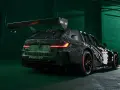 Wyścigowe BMW M3 2025 w kamuflażu, z ogromnym spojlerem i agresywnym dyfuzorem.
