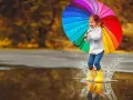 Radosna dziewczynka w żółtych kaloszach skacze po kałużach z tęczowym parasolem. Świetny pomysł, gdzie pojechać z dzieckiem, gdy pada deszcz!