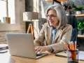Femme souriante travaillant sur son ordinateur portable, planifiant sa future pension pré cheval.