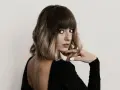 Kobieta z modnym, **blunt bob** w odcieniach brązu i blondu, z grzywką, w czarnej sukience z odkrytymi plecami.