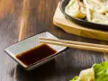 Sos sojowy w miseczce z pałeczkami, obok pierożków gyoza. Szukasz alternatywy, czym zastąpić sos sojowy?