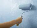 Mano aplica imprimación azul con rodillo a pared texturizada. La imprimación es el primer paso para un acabado perfecto.