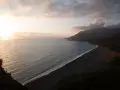 Vue aérienne d'une plage de sable noir bordée par une mer calme et des montagnes embrumées. Ces photos de plage capturent la sérénité d'un paysage côtier au coucher du soleil.