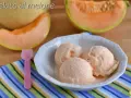 Tre palline di cremoso gelato al melone in una ciotola bianca, con fette di melone fresco sullo sfondo.