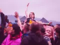 Dziewczyna na rękach tłumu, z podniesionymi ramionami, podczas festiwalu Zew się budzi. Wokół ludzie, niektórzy nagrywają telefonami.
