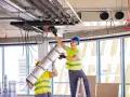 Dwóch pracowników montuje systemy HVAC, instalując izolację na rurach. To kluczowy element zapewniający komfort cieplny.