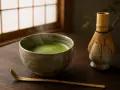 Parzona zielona herbata matcha w ceramicznej miseczce, obok bambusowa miotełka i łopatka.