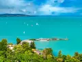 Turkusowe wody jeziora Balaton, pełne żaglówek i statków, z zielonymi wzgórzami w tle.