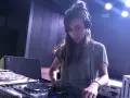 Une dj fille concentrée aux platines, casque sur les oreilles, dans une ambiance tamisée avec des lumières bleues.