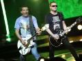 Dwóch członków Kobranocki gra na gitarach podczas koncertu. Jeden w koszulce z orłem, drugi w czarnej z cylindrem i muszką.