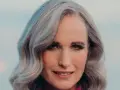 Mujer de 50 años con cabello plateado y ondulado, sonriendo suavemente. Se aprecian las líneas de expresión, reflejo de la flacidez facial a los 50.