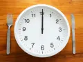 Uhr zeigt 12 Uhr. Gabel und Messer liegen bereit. Zeit für die Mittagspause während der Arbeitszeit.