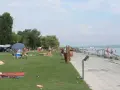 Ludzie odpoczywają na plaży i w wodzie. W tle widać kampery, co sugeruje, że to popularne miejsce na napfeny camping.
