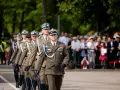 Tomasz Zaręba w mundurze maszeruje w defiladzie wojskowej. W tle widzowie obserwują uroczystość.