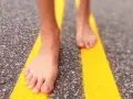 Piedi nudi che camminano su una strada con strisce gialle. Un'esperienza di correre scalzi per sentire la strada.