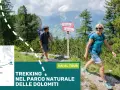Coppia in escursione nel Parco Naturale delle Dolomiti. Un uomo con zaino segue un sentiero, una donna sorride mentre cammina. Segnaletica per il trekking.