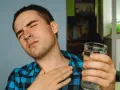 Mężczyzna z bólem gardła, cierpiący na nocny kaszel po alkoholu, sięga po szklankę wody.
