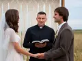 Para młoda trzymająca się za ręce podczas ceremonii ślubnej, z księdzem trzymającym Biblię.