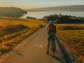 Rowerzysta na ścieżce rowerowej w kierunku jeziora. Złote światło zachodu słońca oświetla malowniczą trasę Velo Czorsztyn.