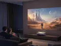 Para ogląda film na wielkim ekranie, gdzie projektor zamiast tv wyświetla futurystyczne miasto na pustyni.