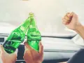 Dwie osoby w samochodzie wznoszą toast zielonymi butelkami piwa.