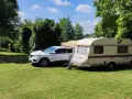 Biały samochód i przyczepa kempingowa na zielonej trawie, otoczone drzewami. Idealne miejsce na **camping smok**.