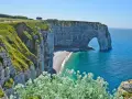 Falaises d'Étretat, France. L'arche naturelle de la Porte d'Aval se dresse fièrement au-dessus de la plage de galets. Le **gr 21** serpente le long de la côte verdoyante.