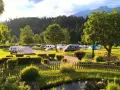 Idyllischer Campingplatz in den Dolomiten mit Wohnmobilen, Zelten und einem Teich.