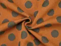Orangefarbener Stoff mit dunklen Punkten, die wie kleine Kreise aussehen. Das Muster ist unregelmäßig und wirkt lebendig.