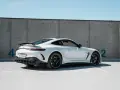 Biały Mercedes GT 63 z czarnym spojlerem i felgami, zaparkowany pod betonową ścianą z niebieskimi cyframi.