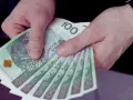 Dłonie trzymają stos banknotów 100 zł. Czy to wystarczy, by pokryć ile wynosi najniższa krajowa?