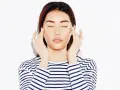 A woman with closed eyes performs a gentle face massage for puffiness, her fingers delicately touching her temples.