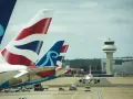 Samoloty z charakterystycznymi ogonami British Airways i innym logo czekają na start na lotnisku Londyn Gatwick. W tle wieża kontroli lotów.