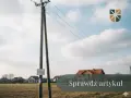 Drewniany słup z przewodami tworzy linię napowietrzną nad polami i domami.