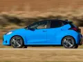 Niebieski hatchback z czarnym dachem pędzi po drodze, za kierownicą siedzi mężczyzna.
