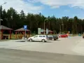 Parking przy lesie, z wiatami i ławkami. W tle las, a na parkingu kilka samochodów. To idealne miejsce na postój w drodze, może nawet w pobliżu **Orlen Sople**.