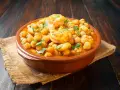 Un plato de barro con garbanzos y langostinos, adornado con perejil fresco, sobre una mesa de madera rústica.