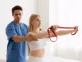 Un chinesiologo, un vero medico, guida una paziente in un esercizio con elastico rosso per migliorare la mobilità.