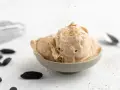 Cremiges Tonkabohnen Eis in einer Schale, bestreut mit gemahlenen Tonkabohnen. Mehrere ganze Tonkabohnen liegen daneben.