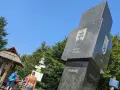 Trójstyk granic Bieszczady: monumentalny obelisk z herbami Słowacji i Ukrainy, obok drewniana wiata i turyści.