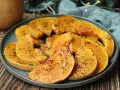 Rodajas de calabaza a la plancha, doradas y especiadas, servidas en un plato azul sobre una mesa de madera.