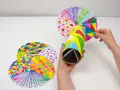 Manos creando manualidades con material reciclado para adolescentes: un caleidoscopio con tubos de cartón y discos decorados con patrones coloridos.